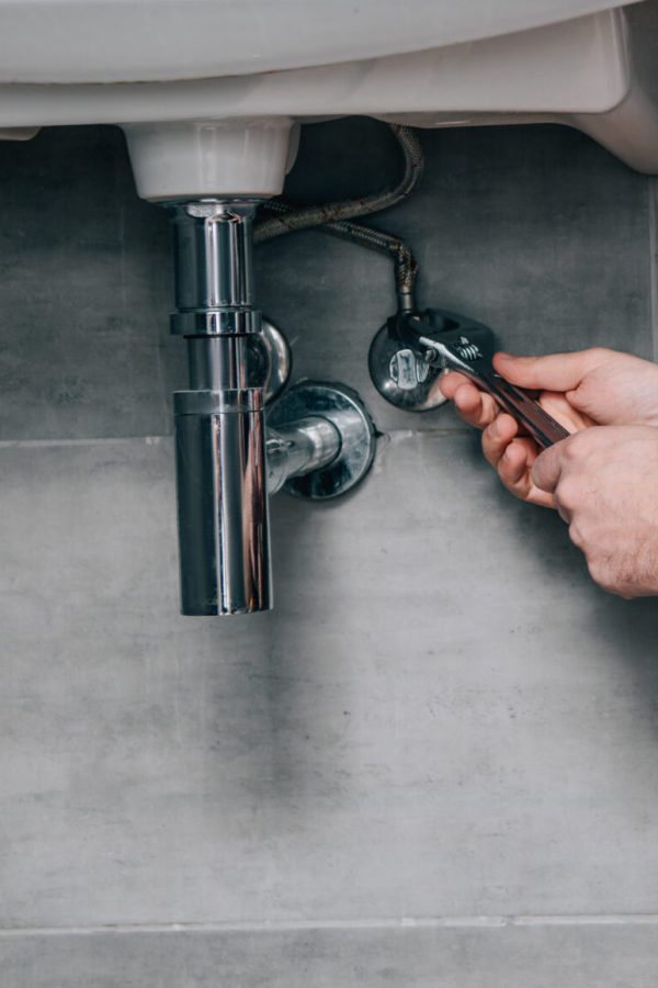 side view of male plumber in working overall fixing sink by spanner in bathroom